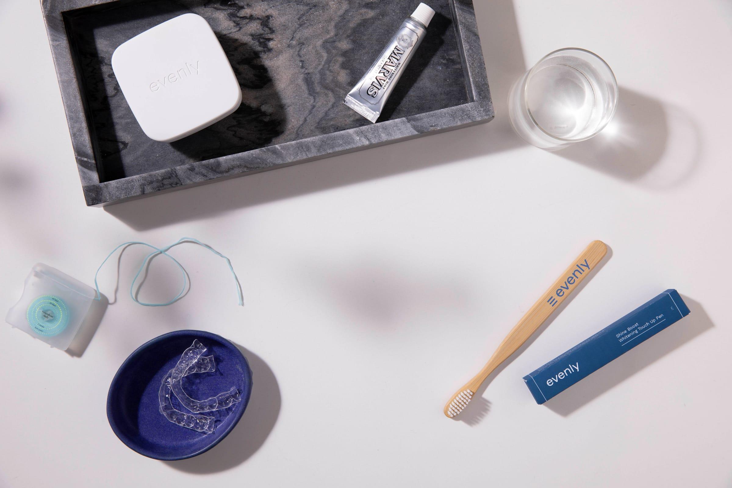 A clear aligner in a small blue dish beside a toothbrush, floss, and a marble tray